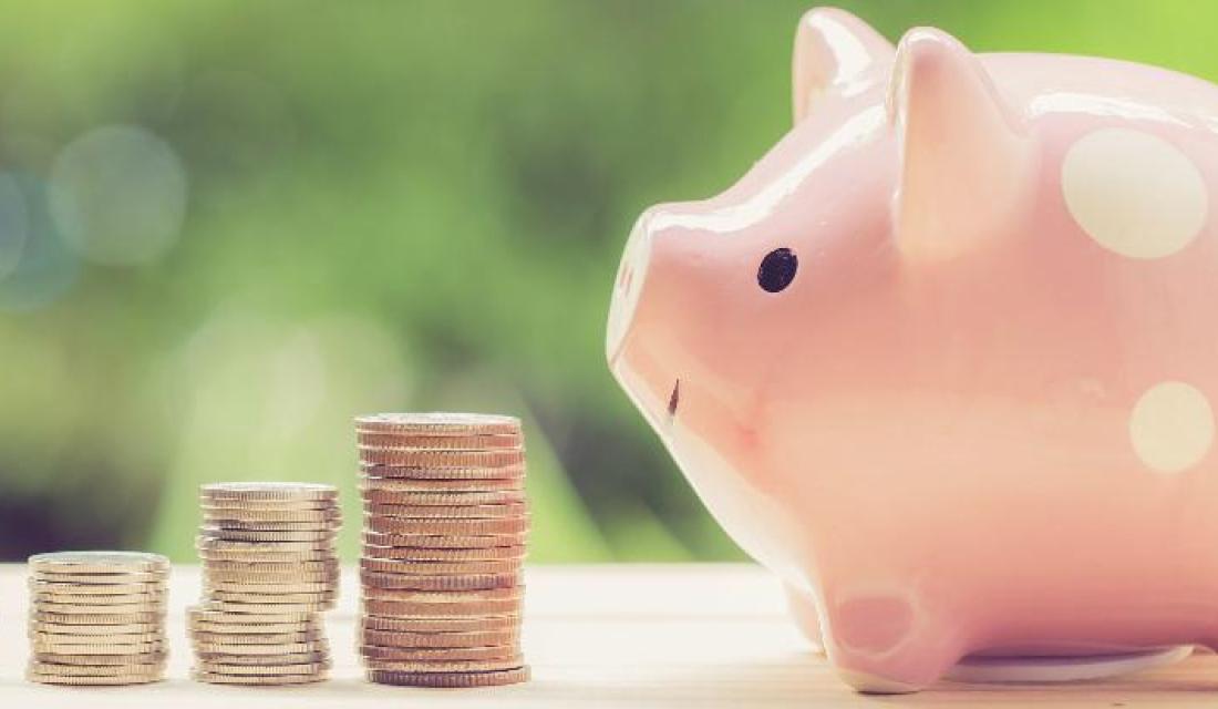 Sparschwein sitzt vor gestapelten Münzen