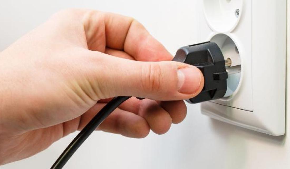 Hand hält Stecker an eine Steckdose