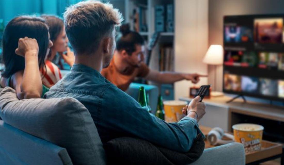 Mehrere Freunde sitzen gemeinsam auf dem Sofa und schauen Fernsehen