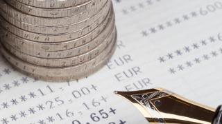 Münzen gestapelt vor Stift und Zettel